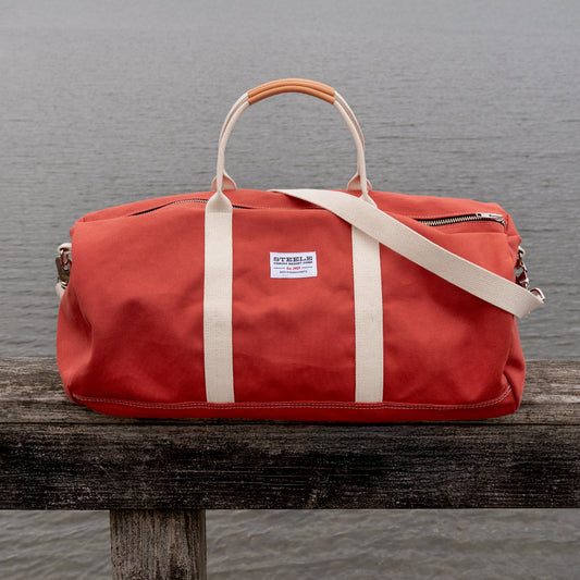 Red duffel bag with a natural canvas strap on a dock