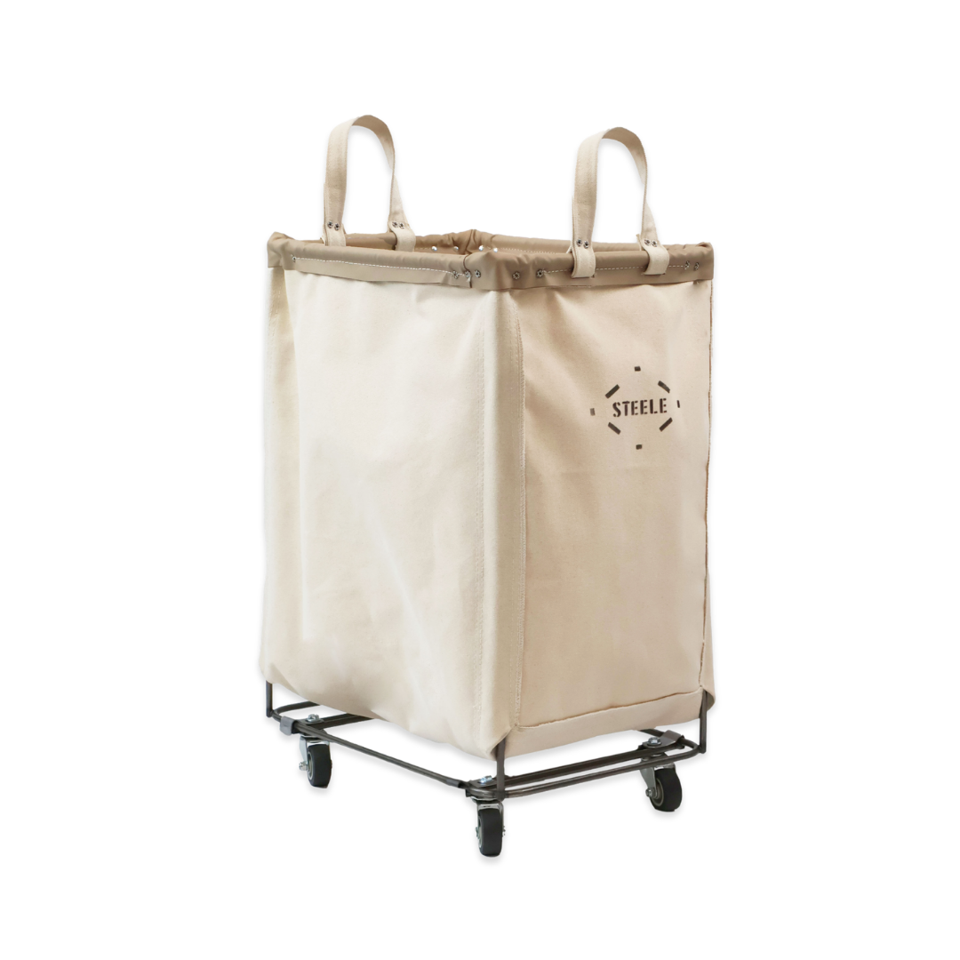A large beige rolling laundry hamper with dual top handles and a black metal rolling cart base, featuring the brand name 'STEEL' printed on the front, set against a plain white background.