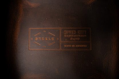 Close-up of a leather product with 'River City' branding on a dark background