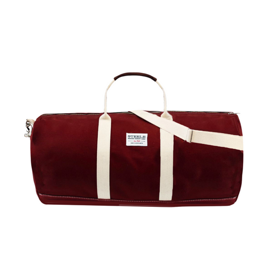 A burgundy canvas duffel bag with cream-colored straps and a white brand label that reads 'STEELE'.
