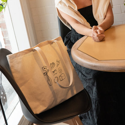Woman sitting at a table with a beige tote bag featuring illustrations.