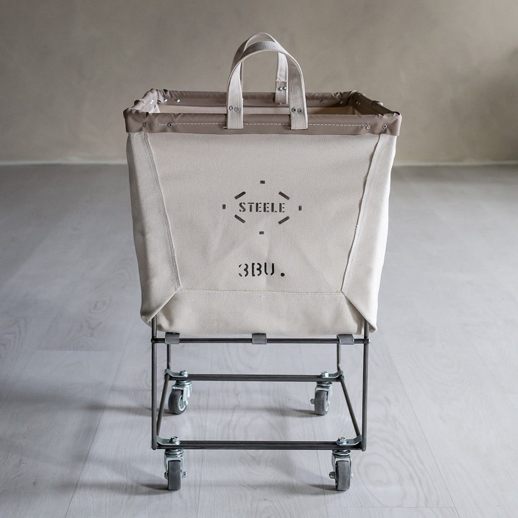 Cart with a large beige bag featuring a brand logo on a plain background