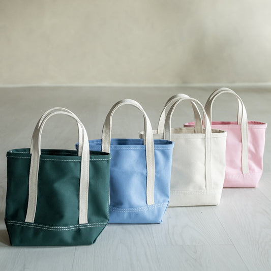 Four tote bags in green, blue, white, and pink on a light surface with a neutral background