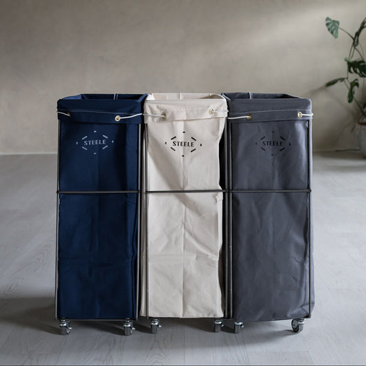 Three laundry baskets in navy, beige, and black with "Steele" branding on a neutral background.