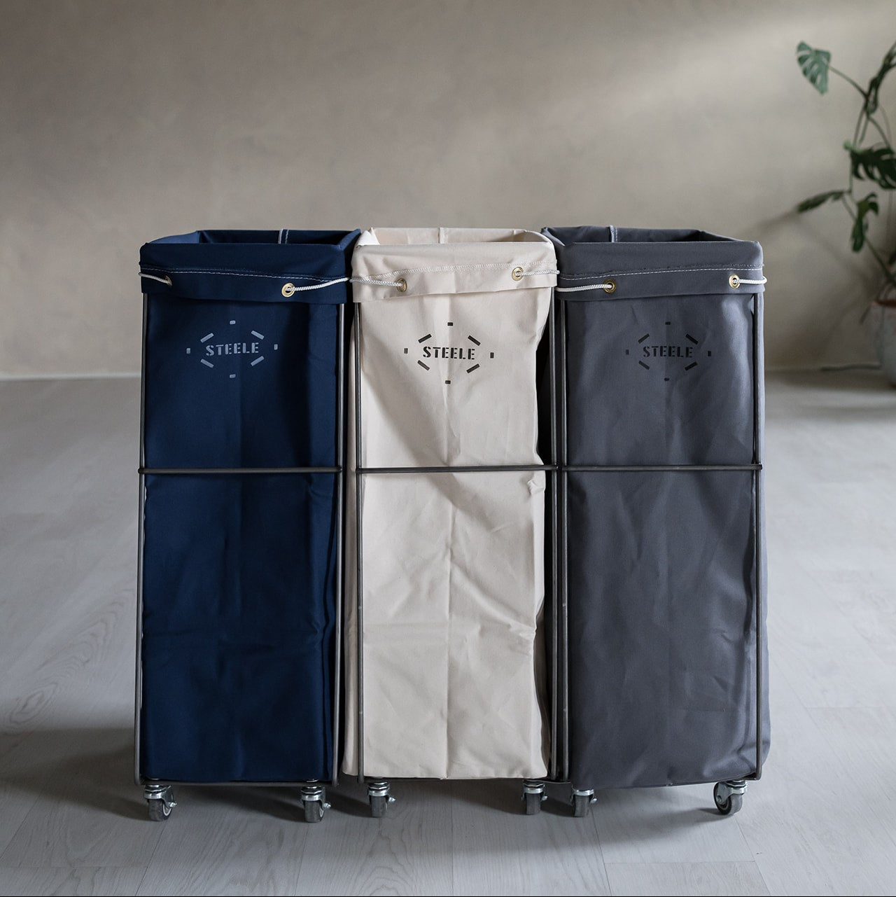 Three laundry baskets in navy, beige, and black with "Steele" branding on a neutral background.