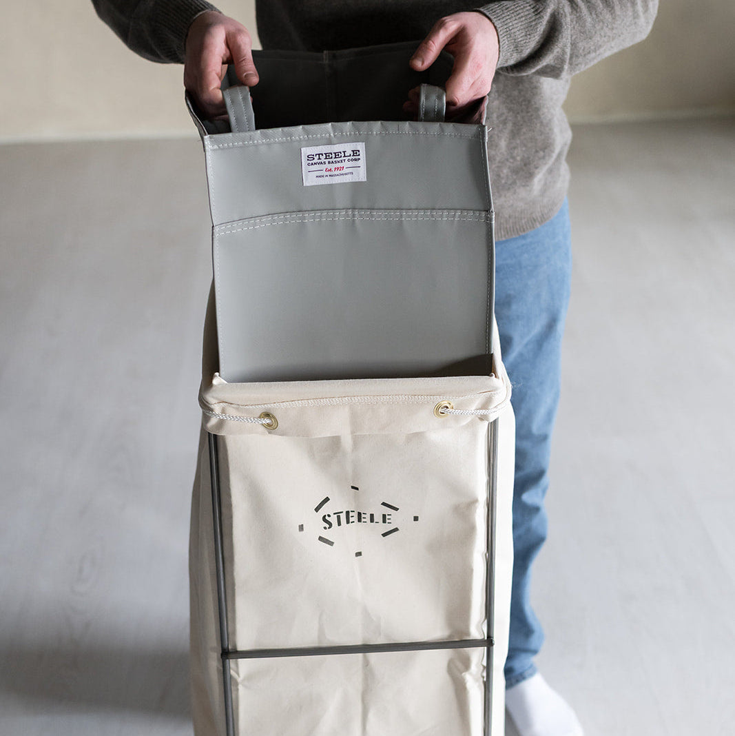Person holding a folded gray bag over a white bag with 'Steele" branding on a light background