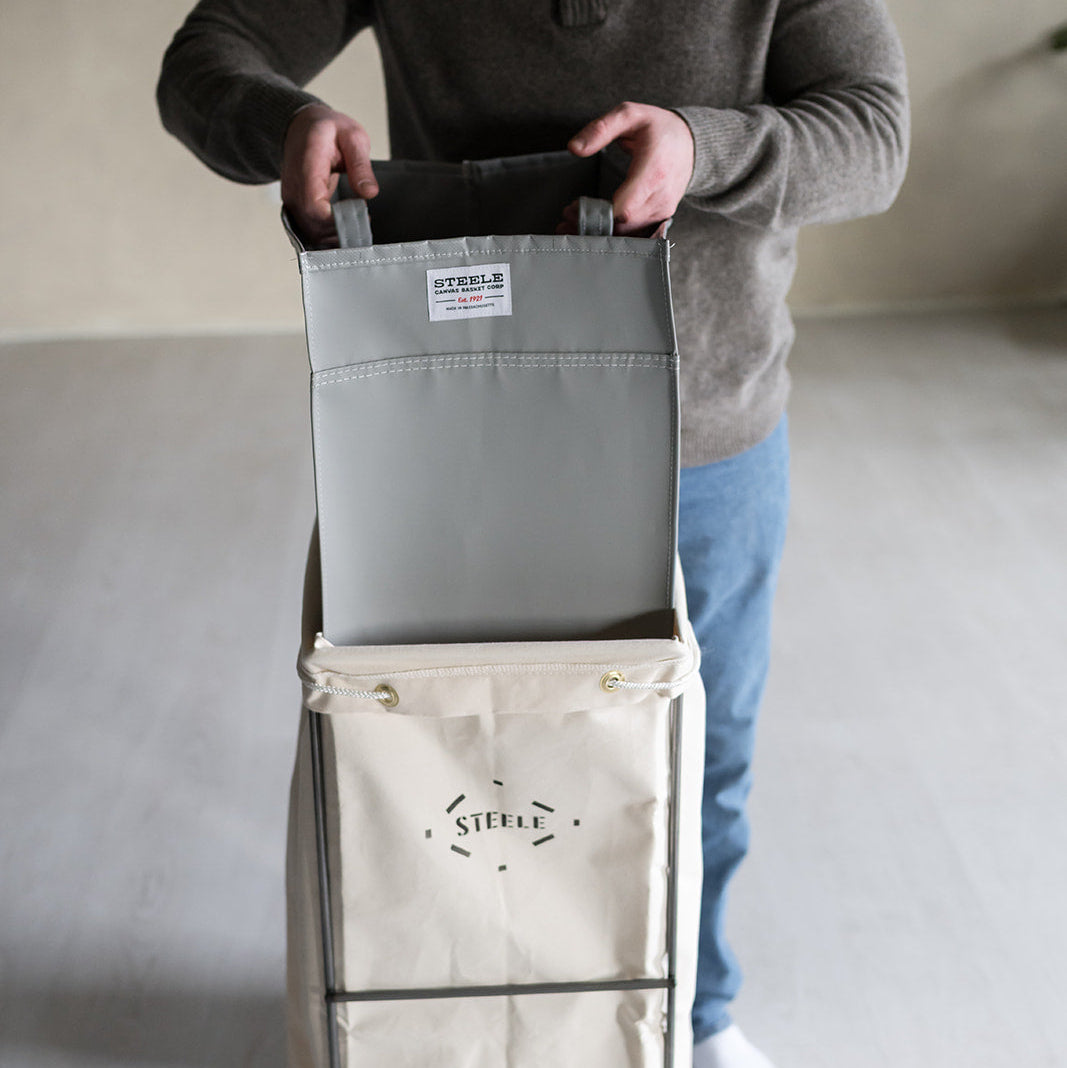Person holding a gray bag on a rolling cart with 'Steele' branding.