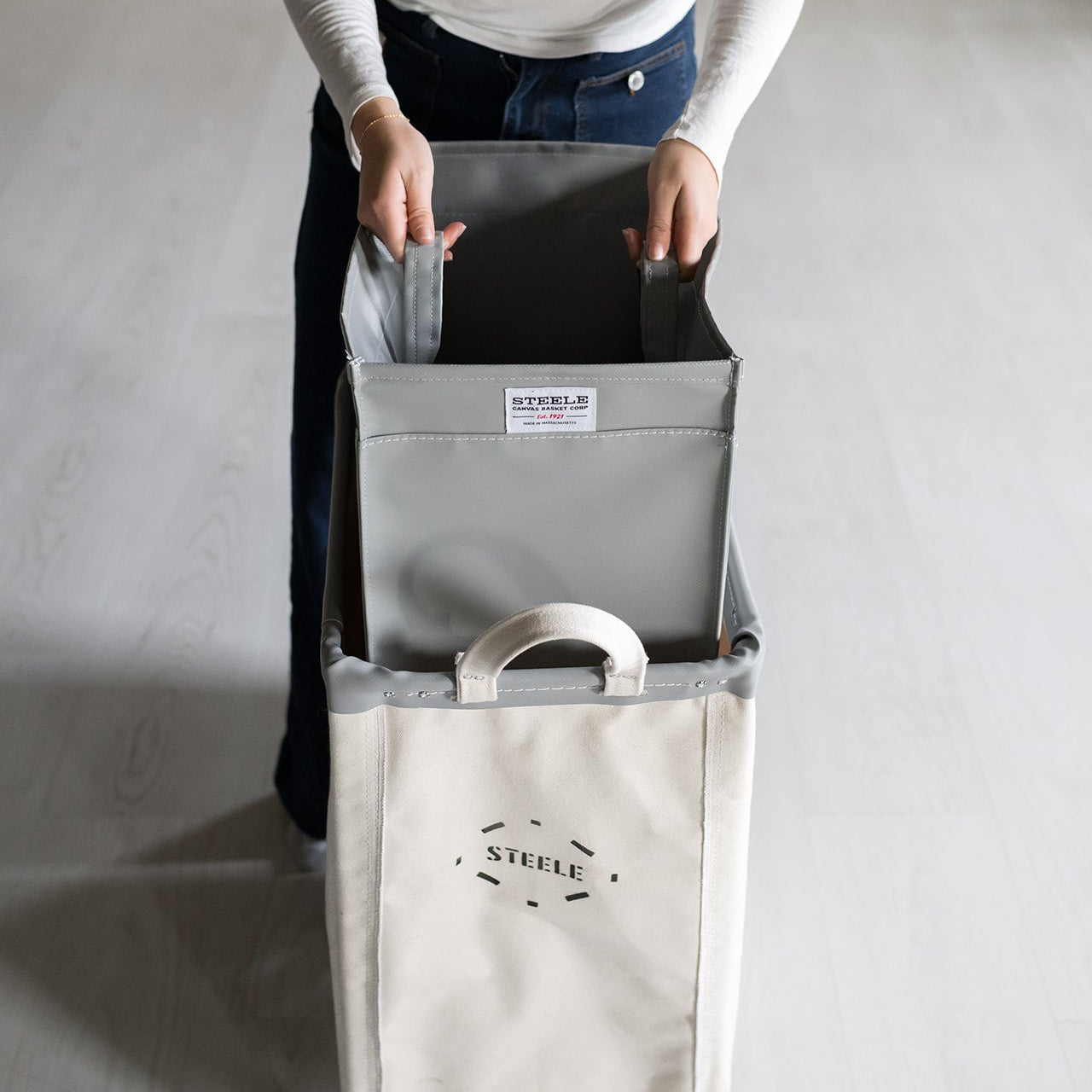Person holding a gray laundry basket with a white label on a light gray background
