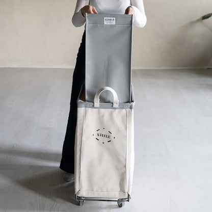 Woman holding a large gray bag with a cart in a minimalistic setting