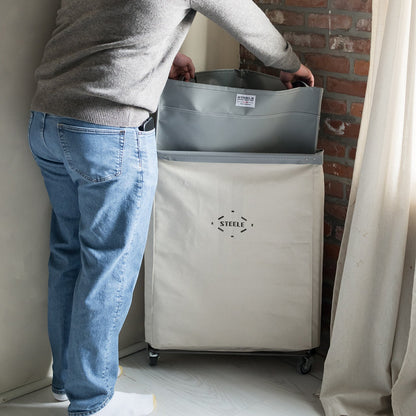 Person lifting a laundry liner out of a beige storage unit with 'Steele' branding.