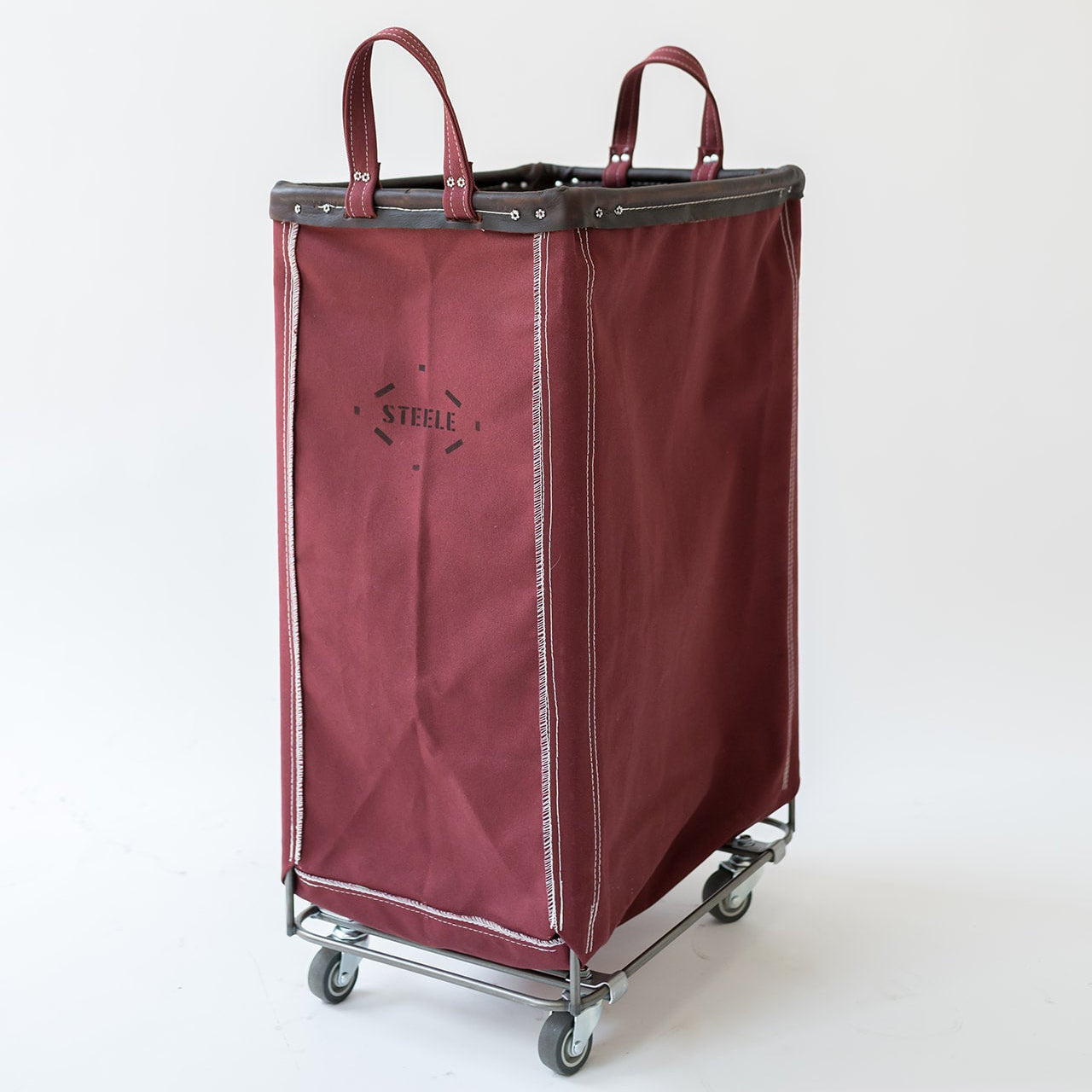 A burgundy fabric laundry hamper with dark gray trim and handles, mounted on a metal rolling cart with gray wheels. The brand name 'STELLE' is printed on the front.