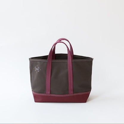 A dark brown canvas tote bag with a deep burgundy base and matching burgundy handles, shown against a plain white studio background.