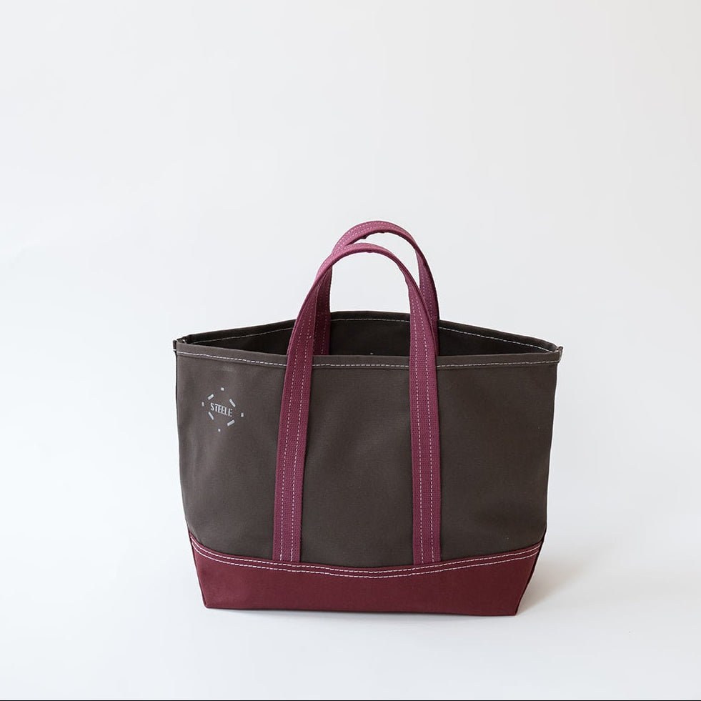 A dark brown canvas tote bag with magenta-pink leather handles and a matching magenta-pink bottom base, shown against a plain white background.