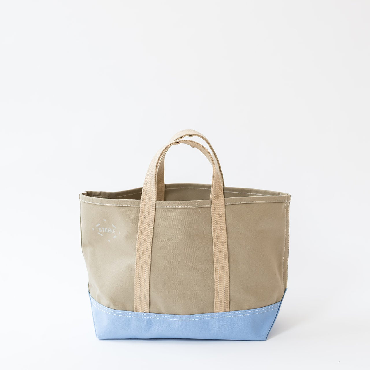 A canvas tote bag with a beige body, light beige handles, and a light blue bottom base, shown against a plain white background.