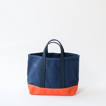 A navy blue canvas tote bag with a bright orange bottom panel and matching dark blue handles, shown on a clean white background.
