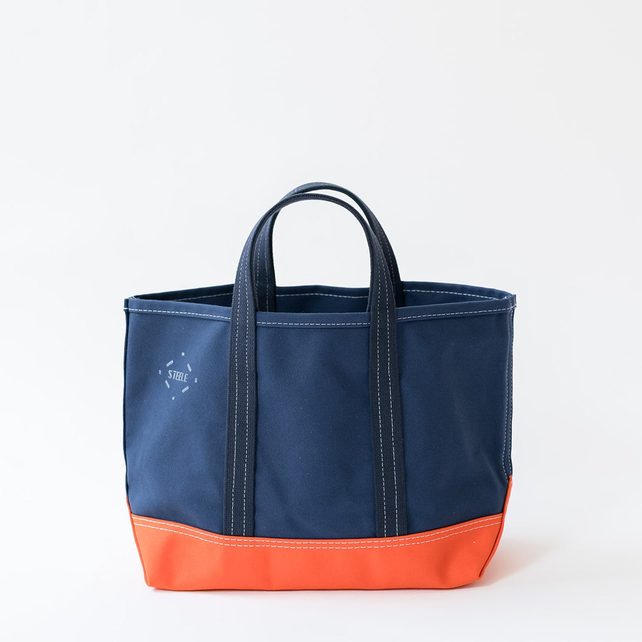 A color-blocked canvas tote bag with a navy blue upper body and a bright orange bottom base, featuring dark navy handles and a small white circular logo on the front left.