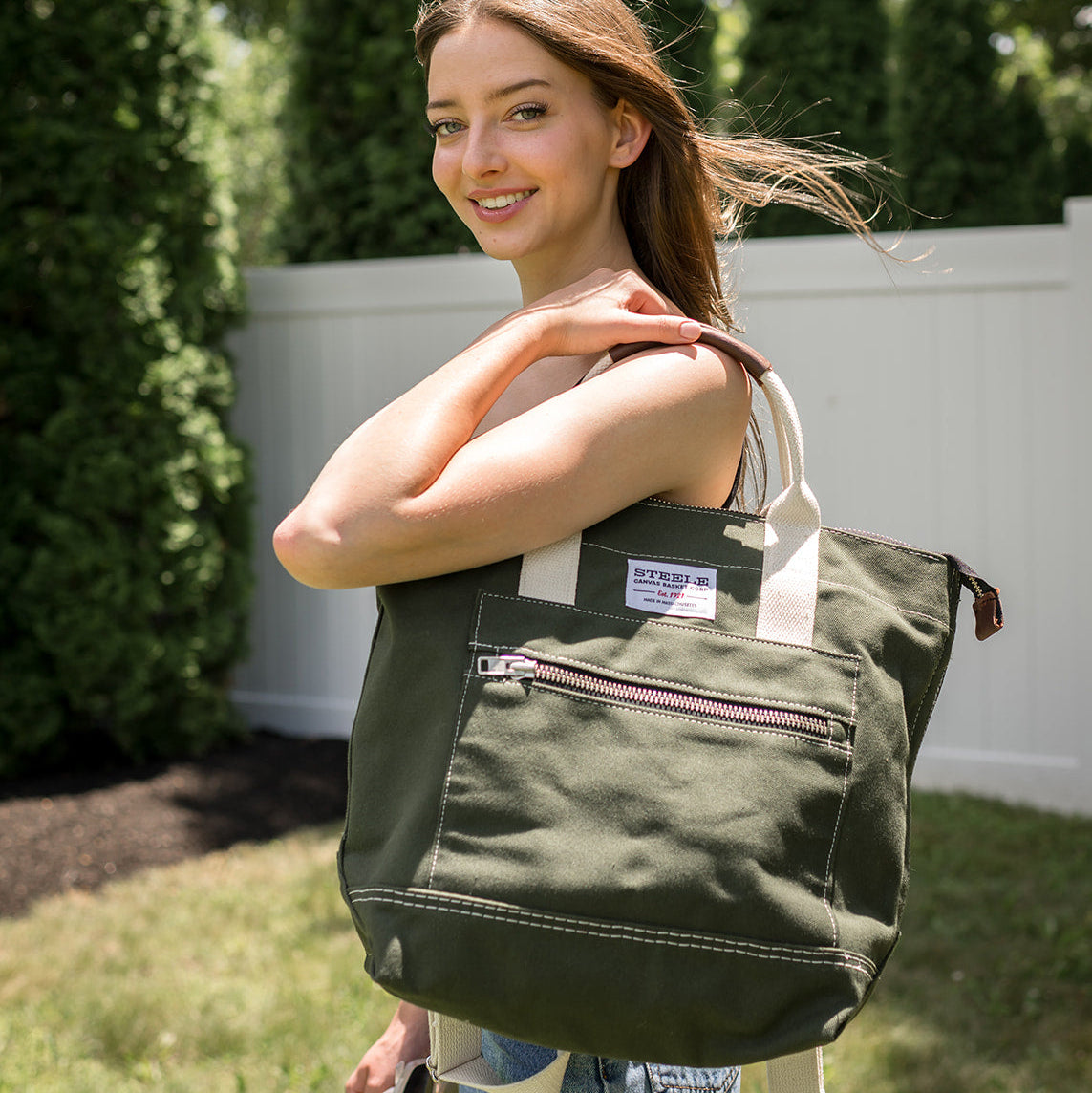Woman holding a green tote bag outdoors with trees in the background