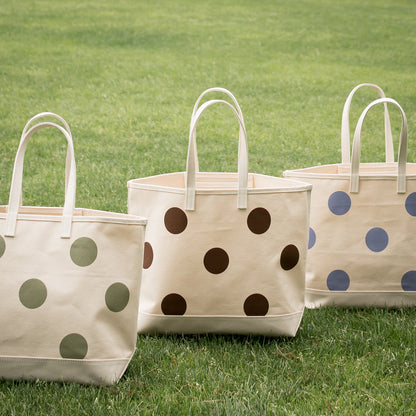 Three tote bags with polka dot patterns on a grassy background
