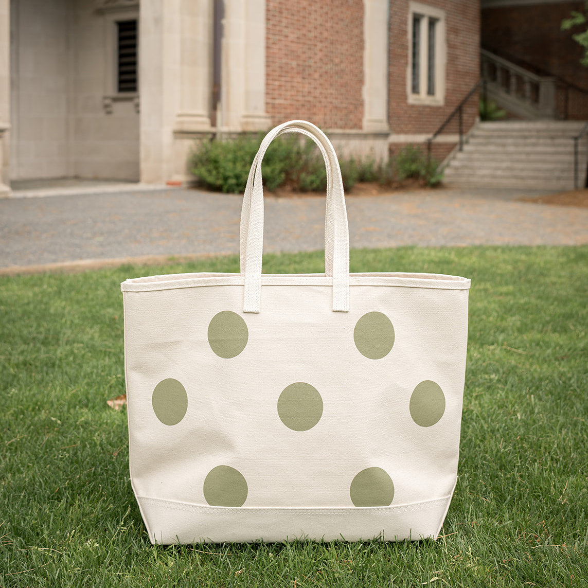 White tote bag with green polka dots on grass in front of a building