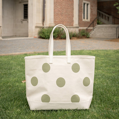 White tote bag with green polka dots on grass in front of a building