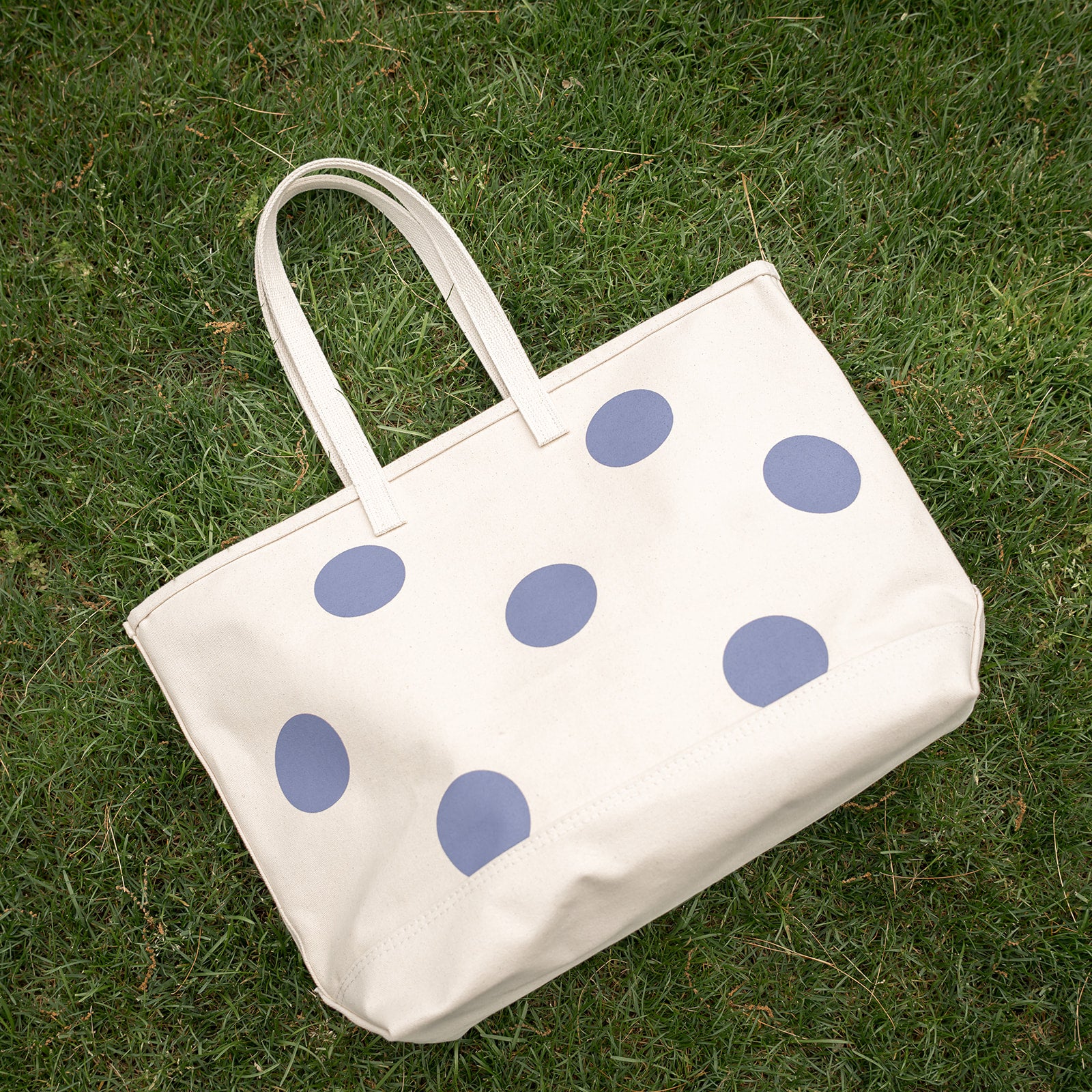 White tote bag with blue polka dots on grass