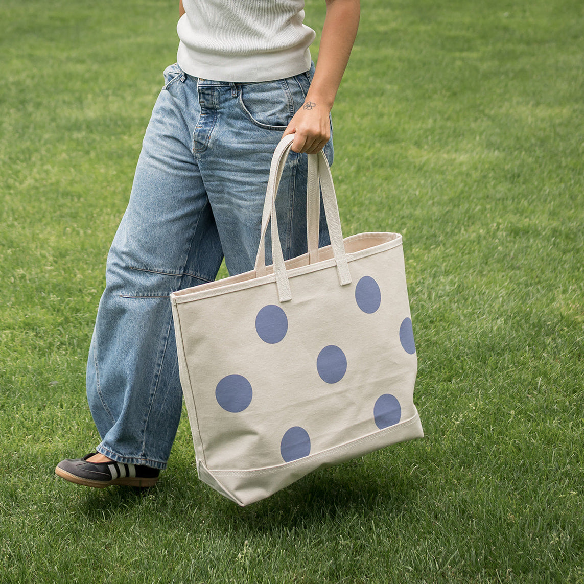 Person holding a tote bag with blue polka dots on a grassy field