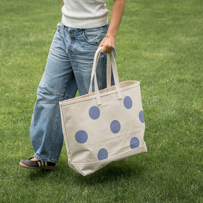 Person holding a tote bag with blue polka dots on a grassy field