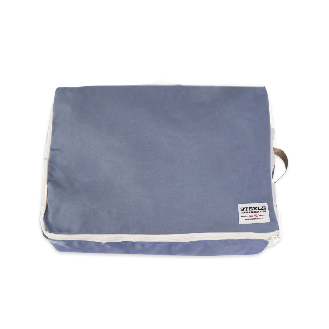 A rectangular steel blue canvas pouch with white piping and a small white brand label on the bottom right, shown on a plain white background.