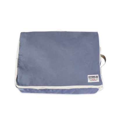 A rectangular steel blue canvas pouch with white piping and a small white brand label on the bottom right, shown on a plain white background.
