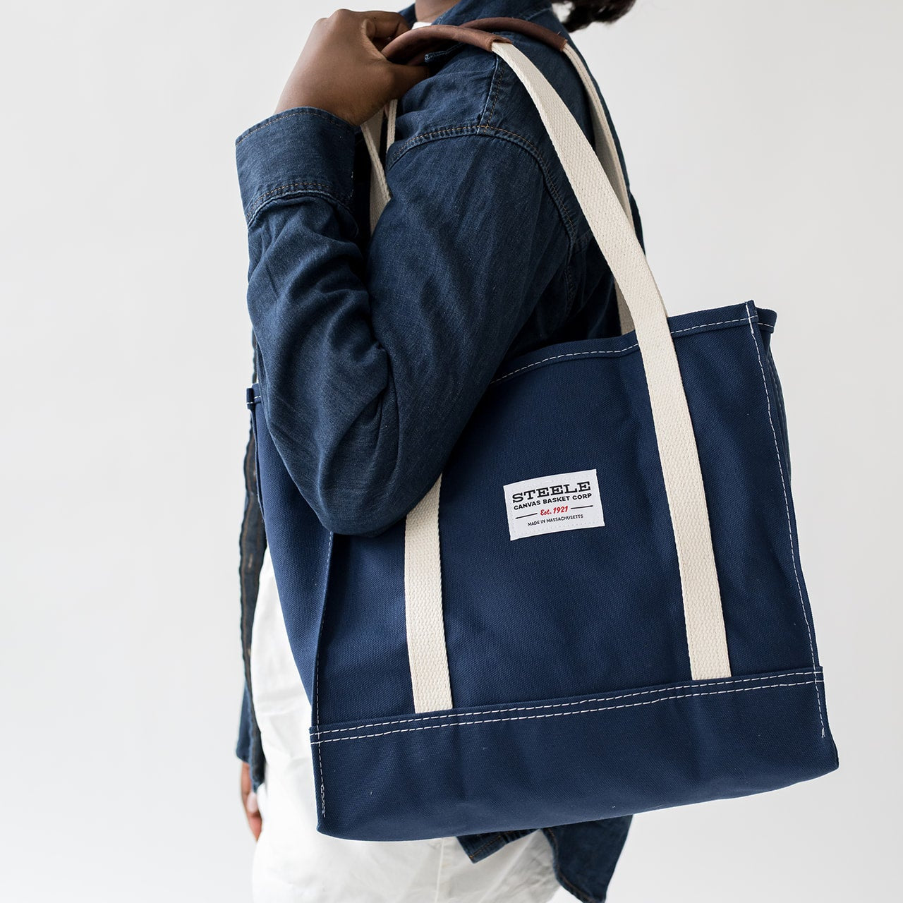 Person holding a navy tote bag with white straps on a plain background
