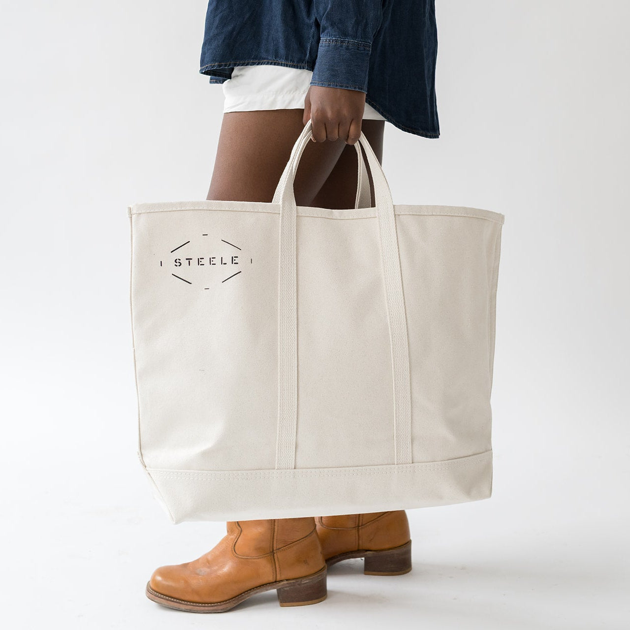 Person holding a beige tote bag with 'Steele' branding on a white background