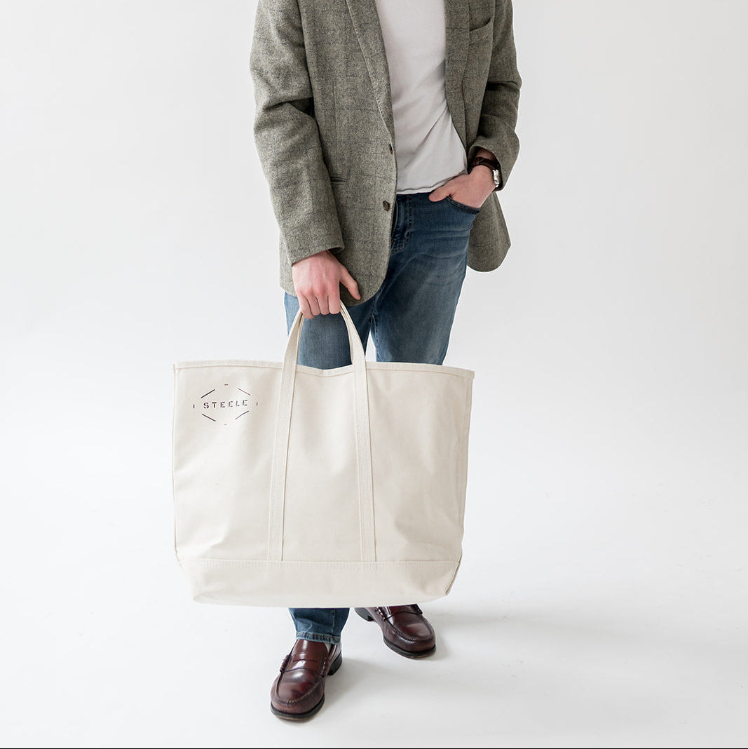 Man holding a white tote bag against a plain background