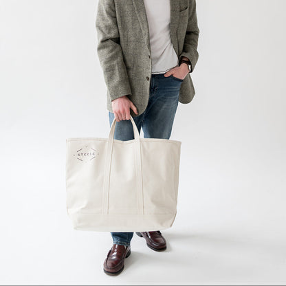 Man holding a white tote bag against a plain background