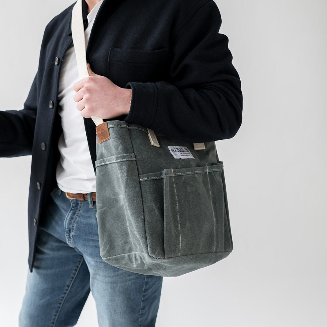 Person holding a gray shoulder bag against a plain background