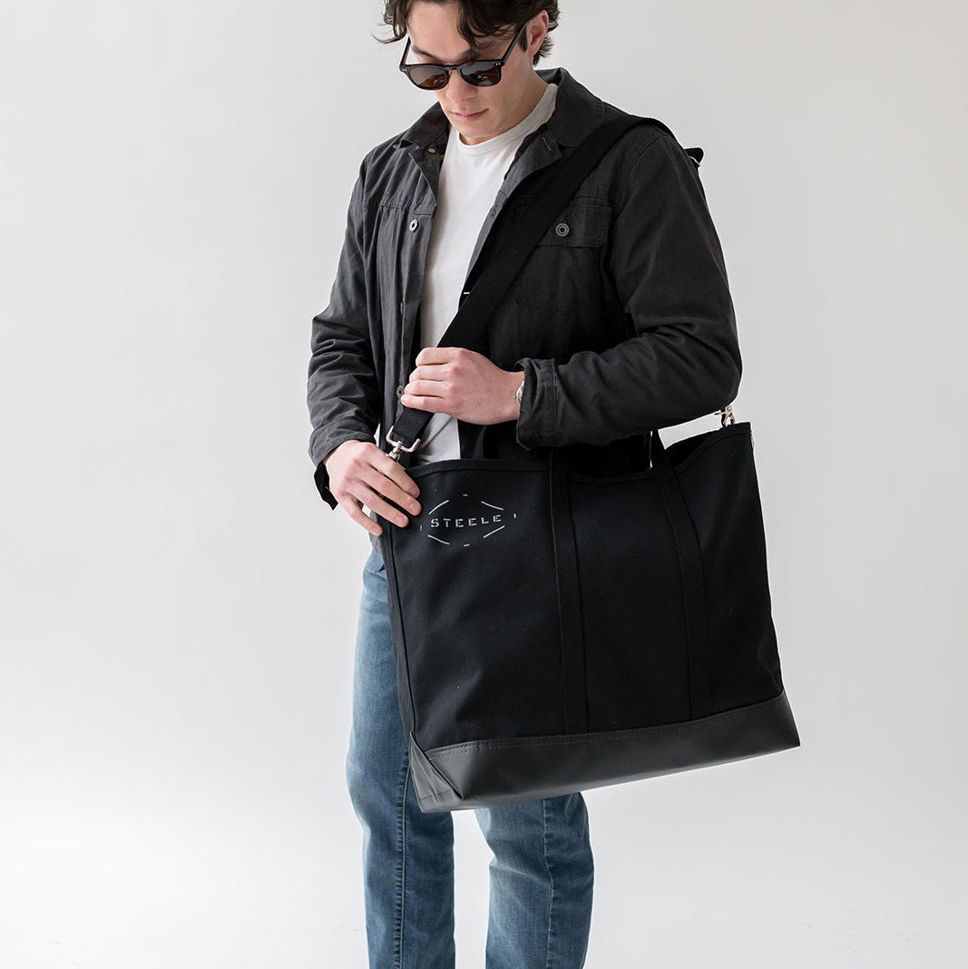 Man holding a black tote bag against a white background