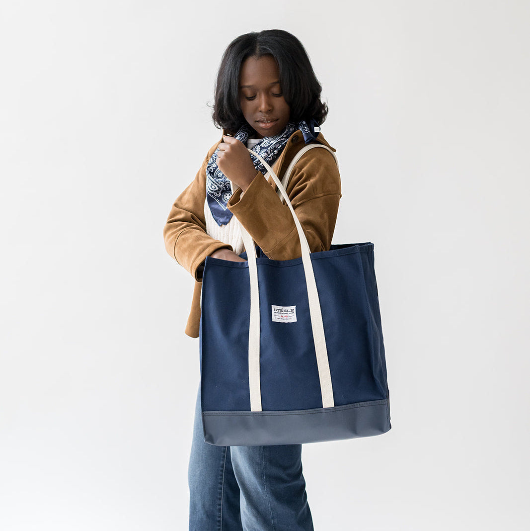 Person holding a navy tote bag with white handles on a white background
