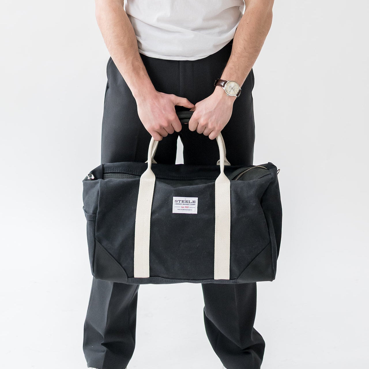 Person holding a black duffel bag with white straps on a white background