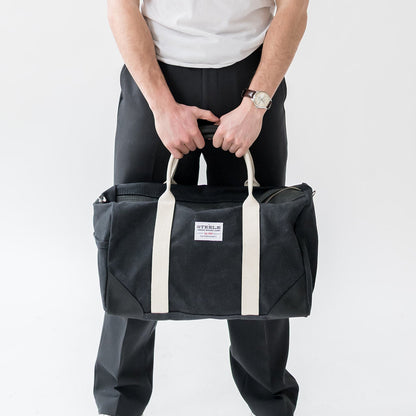 Person holding a black duffel bag with white straps on a white background