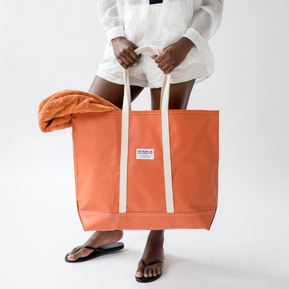 Person holding an orange tote bag with a visible brand label on a white background