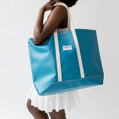 Woman holding a blue tote bag with a white strap against a plain background