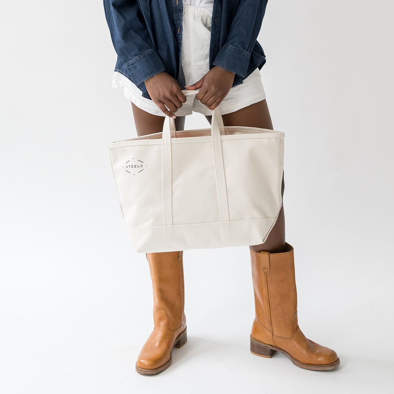 Person holding a white tote bag with a visible brand logo on a white background