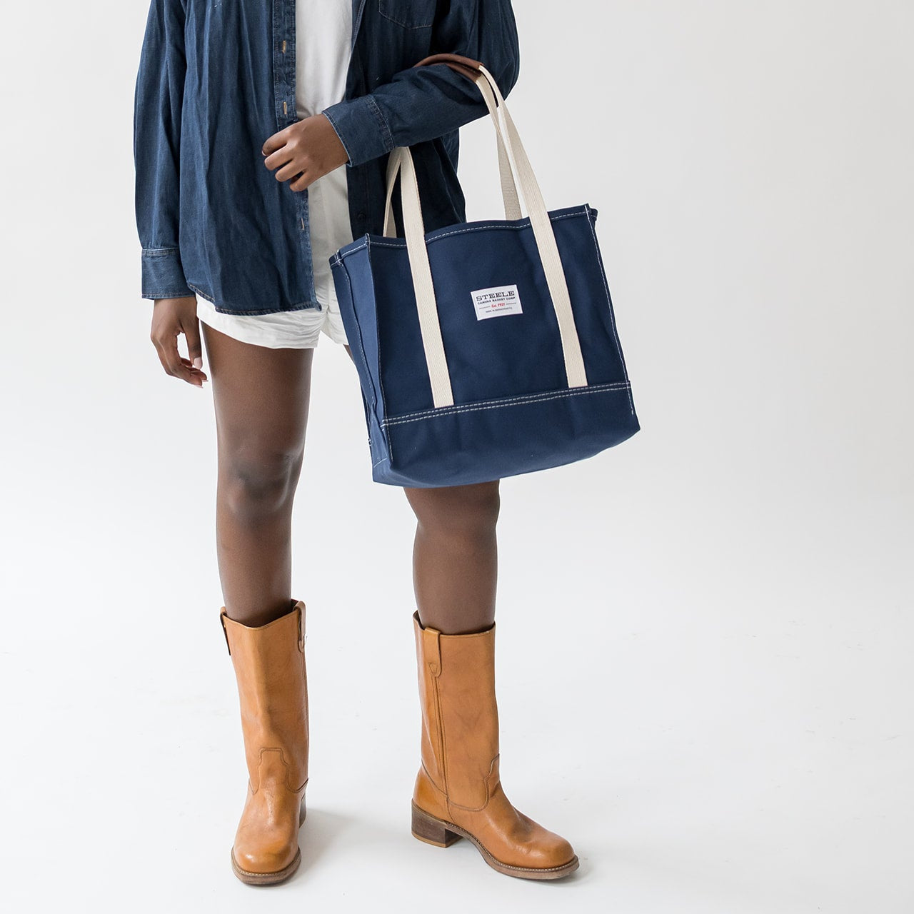 Person holding a navy tote bag with a white label on a white background