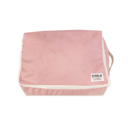 A pink zippered travel packing cube with white piping and a small white brand label on the front, shown on a plain white background.