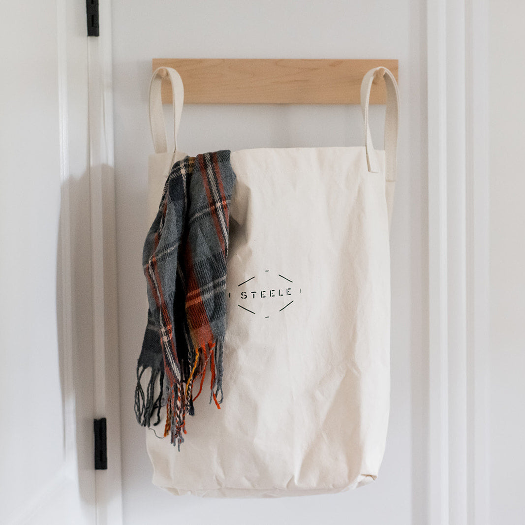 canvas tote bag with plaid scarf hanging on a wooden rack against a white wall.