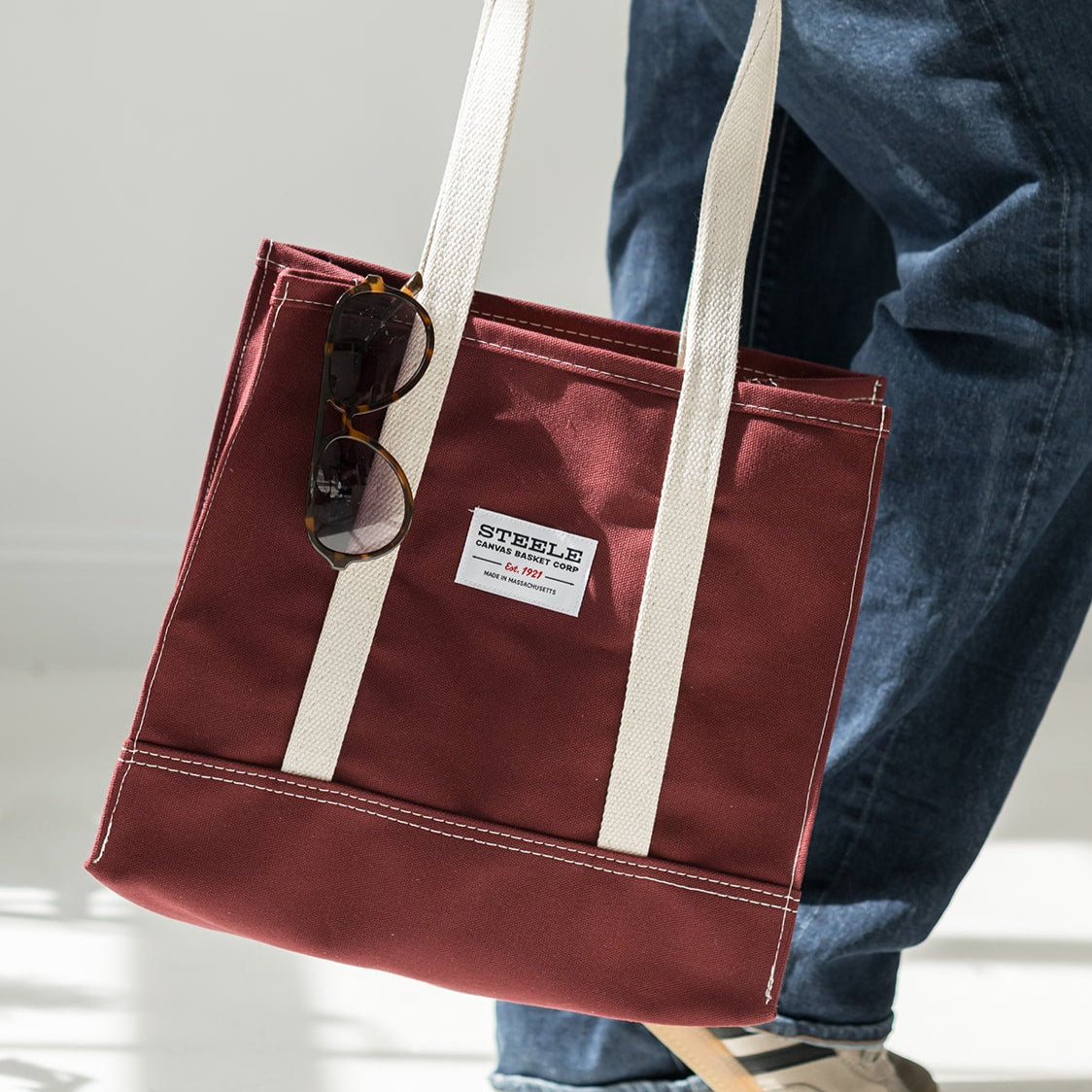 Person holding a maroon tote bag with a visible brand label on a light background