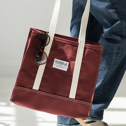 Person holding a maroon tote bag with a visible brand label on a light background