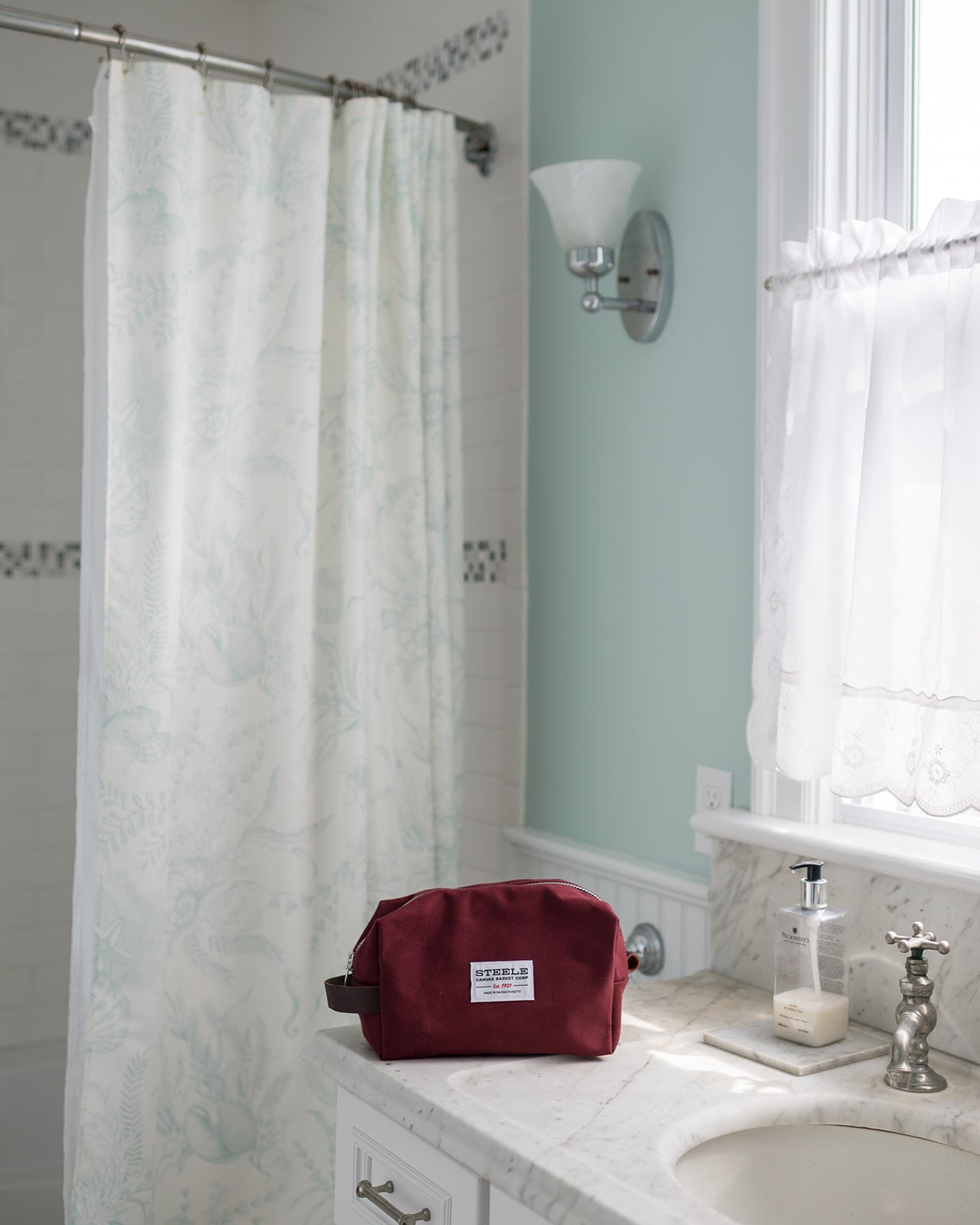 Bathroom with a maroon toiletry bag on a counter, shower curtain, and sink.