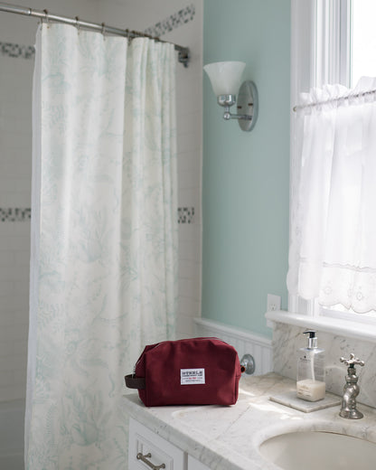 Bathroom with a maroon toiletry bag on a counter, shower curtain, and sink.