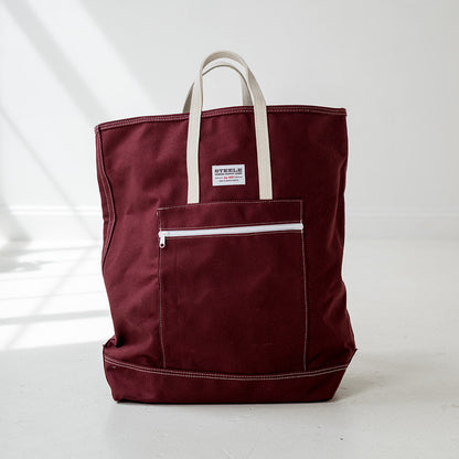 Maroon tote bag with white handles on a light gray background