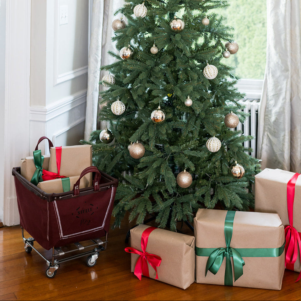 Decorated Christmas tree with presents and a cart in a room with large windows.